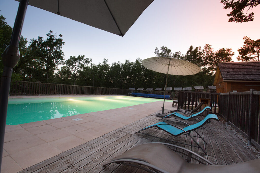 Détente au cœur du Lot : la piscine du Bois de Faral invite à la relaxation en lisière de forêt, face aux chalets de bois