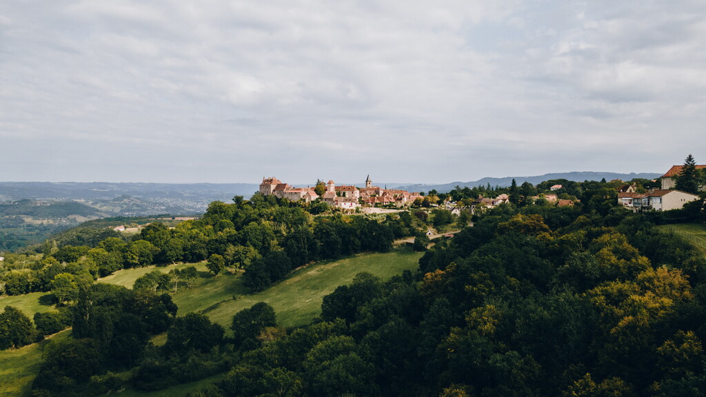 Vue panoramique sur Saint-Cirq-Lapopie, joyau médiéval du Lot nichée dans un écrin de verdure et de collines ondulantes